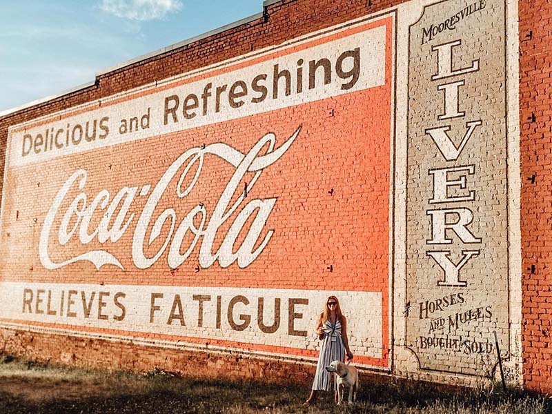 woman and dog in front of a coca-cola mural downtown Mooresville